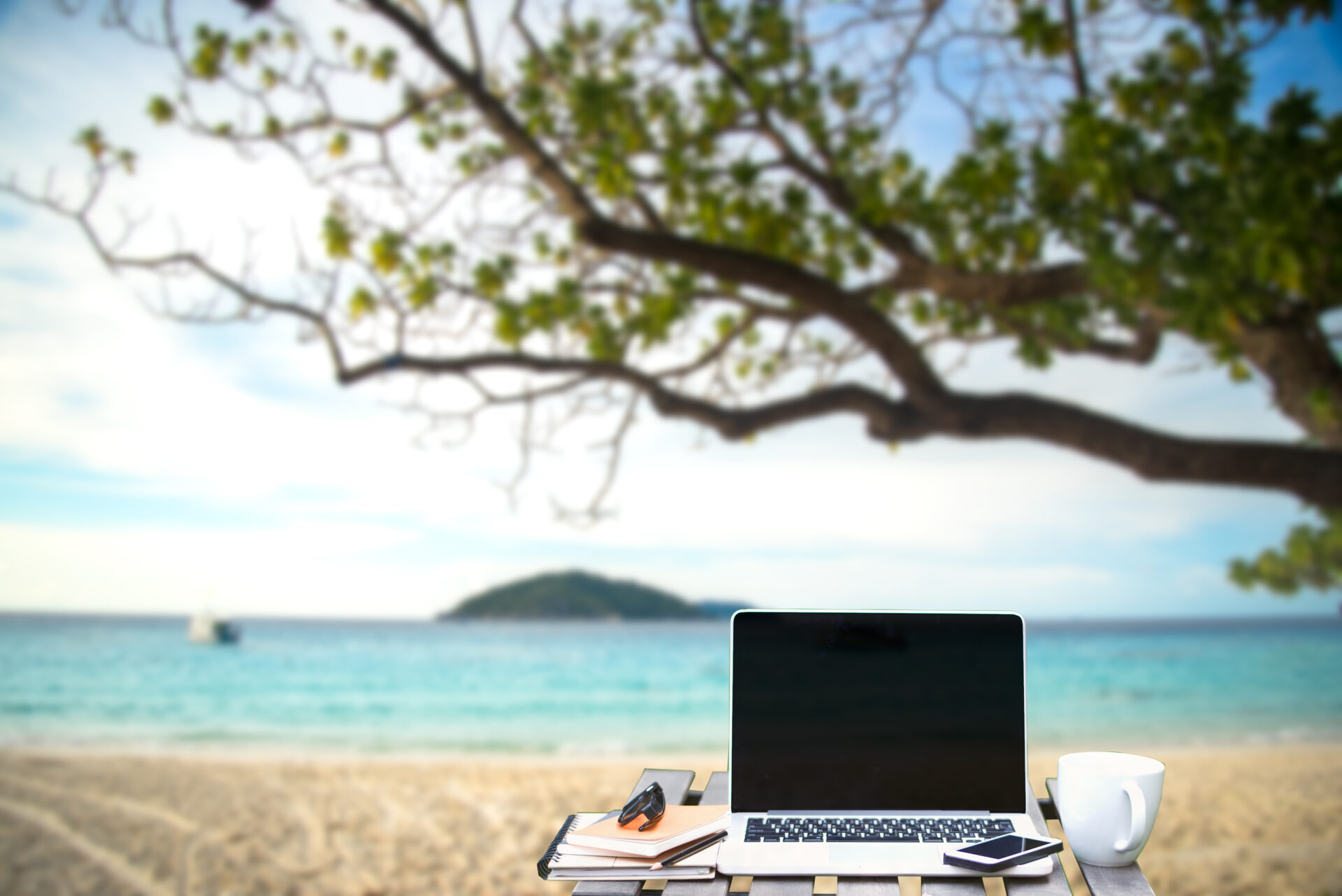 A laptop on the beach with a view of water